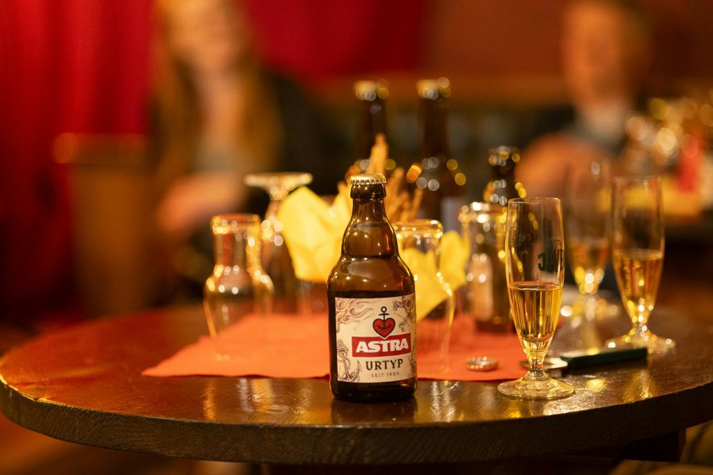 다양한 유리잔과 병이 놓인 탁자 위에 놓인 아스트라 맥주 한 병. 배경이 흐릿합니다.