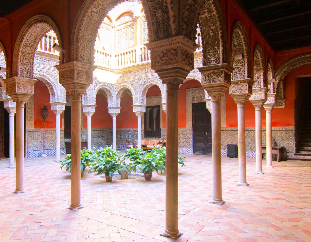 화려한 아치, 타일 바닥에 화분, 밝은 자연광 아래 장식된 벽이 있는 마당입니다.