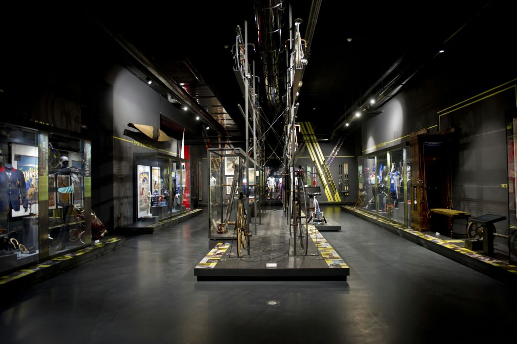 중앙 금속 조각이 있는 유리 케이스의 다양한 디스플레이와 유물을 전시하는 희미한 조명의 박물관 갤러리입니다.