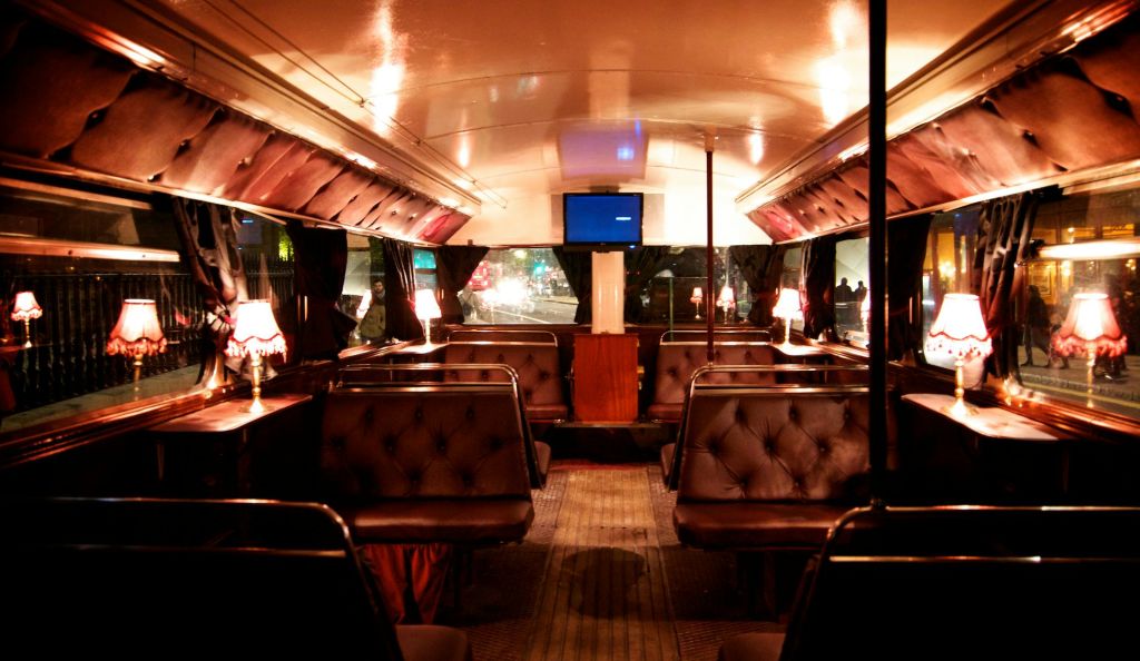 가죽으로 장식된 좌석 부스, 작은 테이블 램프, 전면 벽에 설치된 TV가 있는 빈티지 버스 내부.