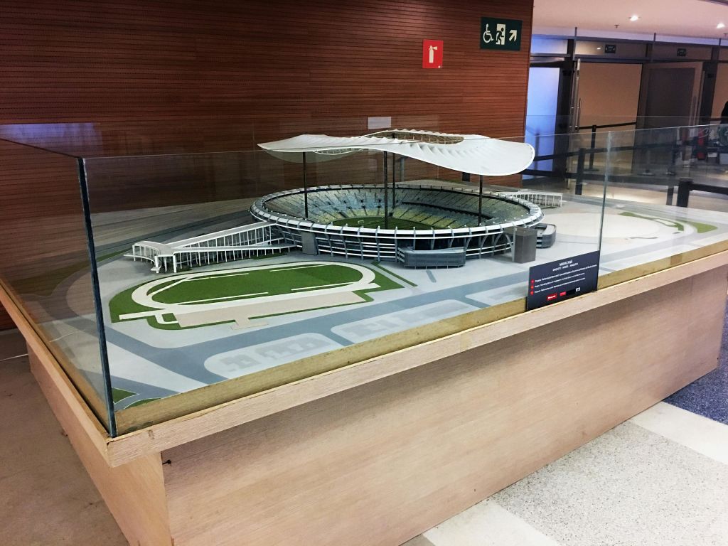 실내에 유리 디스플레이 케이스로 둘러싸인 좌석, 트랙, 독특한 물결 모양 지붕이 있는 경기장의 상세한 스케일 모델.