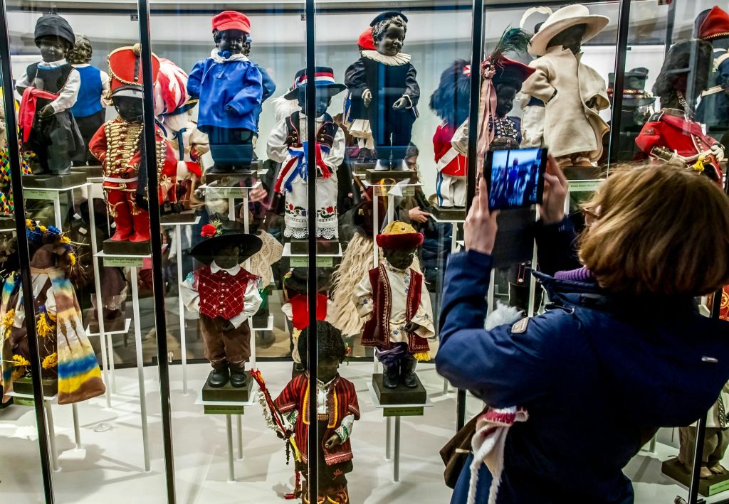 한 사람이 유리 케이스 뒤에 다양한 문화 의상을 입은 다양한 전통 인형이 전시된 박물관을 촬영하고 있습니다.