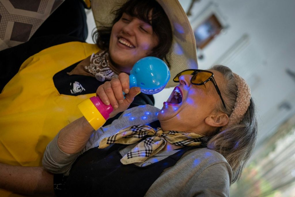 두 여성이 즐거워하고 있습니다. 한 여성은 장난감 마이크에 노래를 불렀고, 두 여성은 모두 미소를 지었습니다. 모자와 화려한 액세서리를 착용합니다.