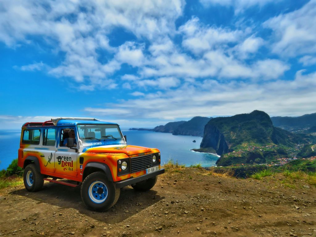 푸른 하늘과 험준한 절벽을 배경으로 아름다운 해안 풍경이 내려다보이는 절벽에 주차된 화려한 4X4 차량입니다.