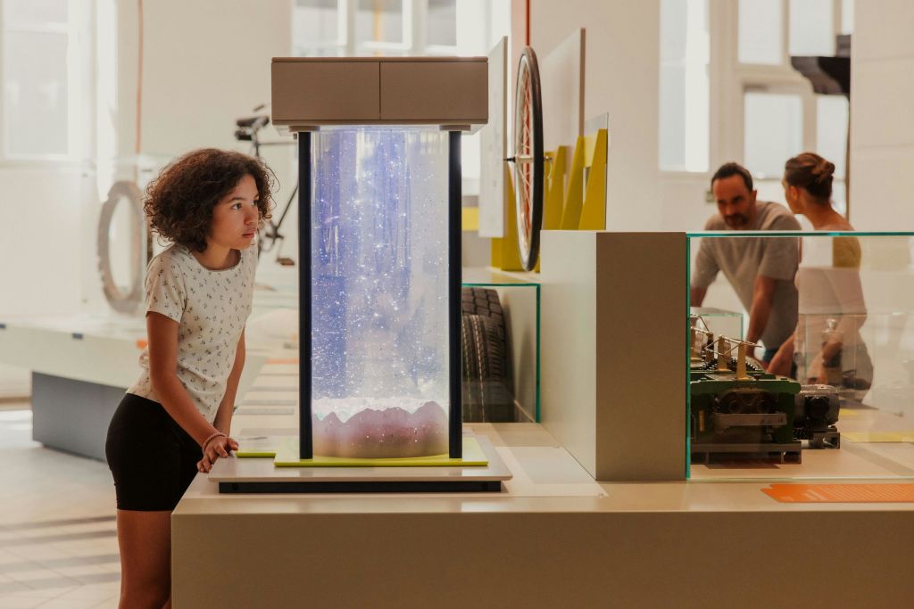 곱슬머리를 한 사람이 밝고 현대적인 전시 공간에서 조명이 켜진 디스플레이 케이스를 바라보고 있습니다.