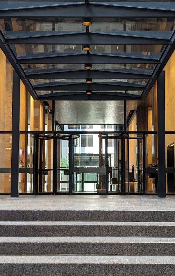 회전문과 유리 캐노피가 있는 현대적인 유리 입구가 밝은 인테리어의 건물로 이어집니다.