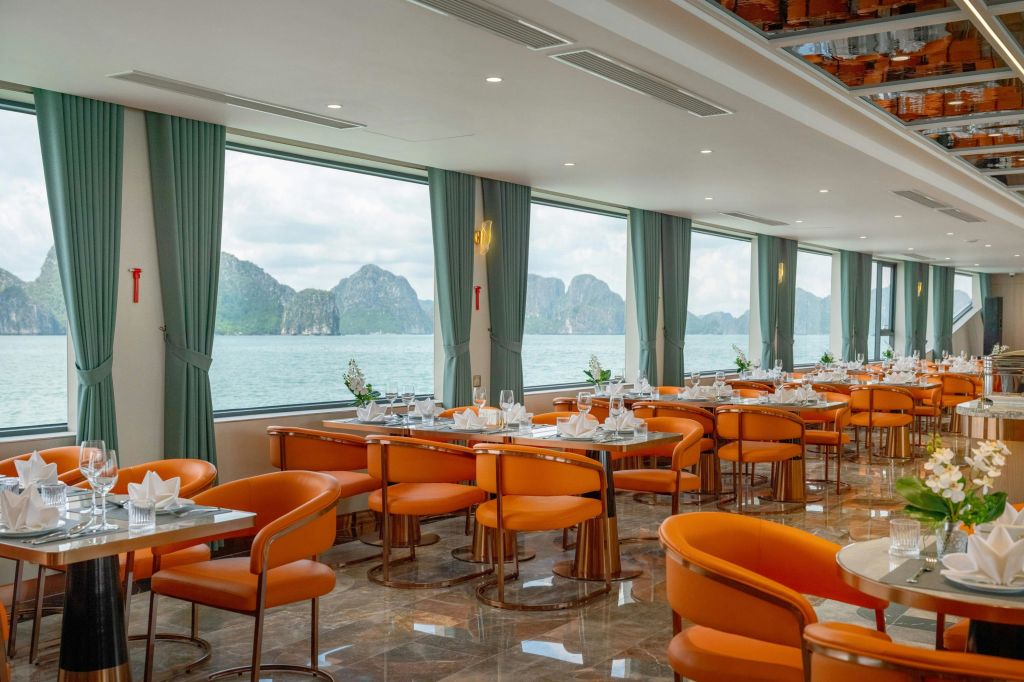 오렌지색 의자, 깔끔하게 세팅된 테이블, 물 너머로 보이는 산의 경치를 감상할 수 있는 커다란 창문이 있는 현대적인 식사 공간.