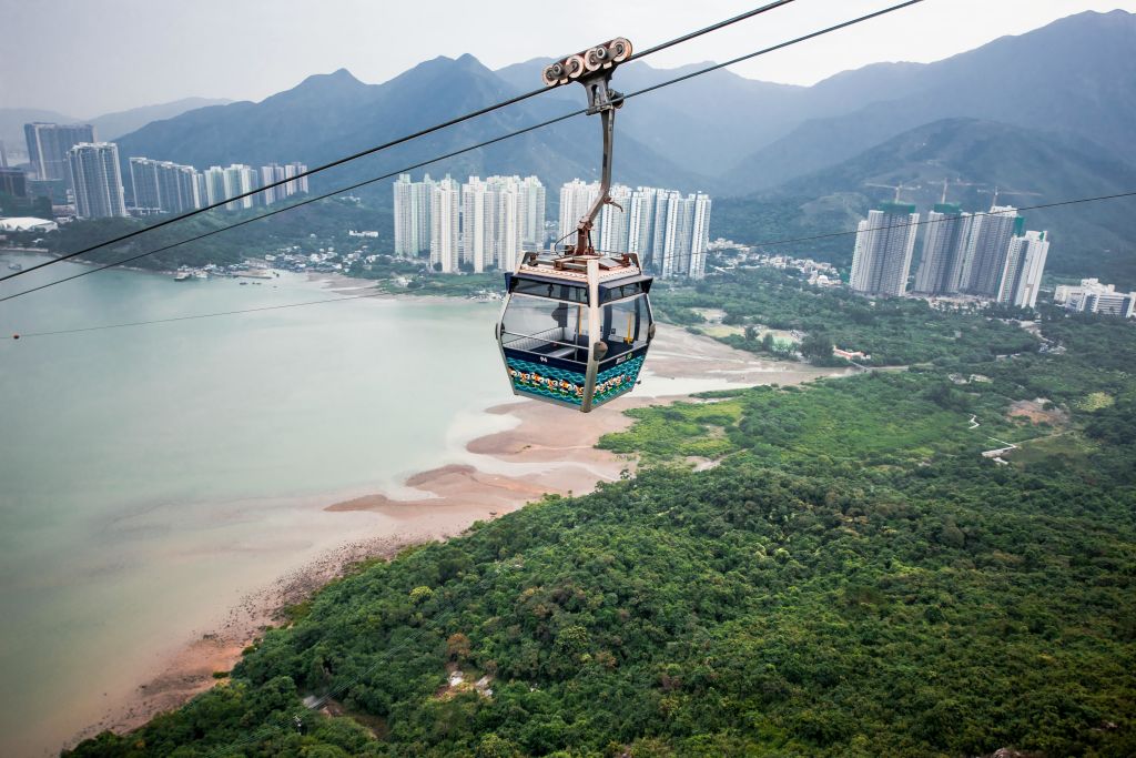 높은 건물과 산을 배경으로 푸른 숲과 만 위로 케이블카가 운행됩니다.
