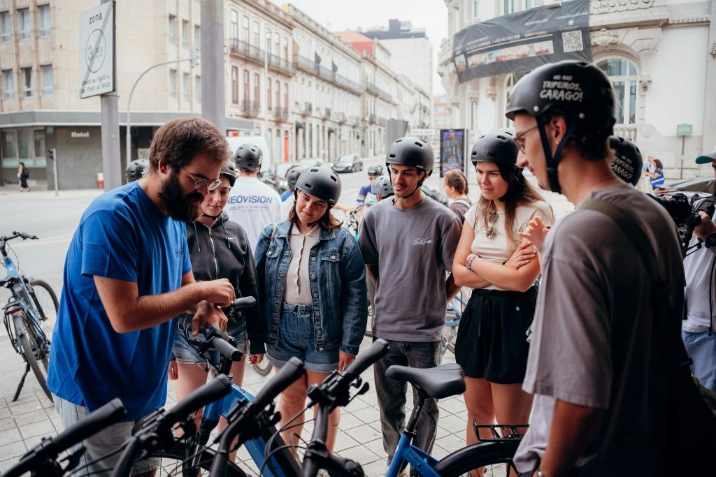 헬멧을 쓰고 자전거 근처에 서 있는 한 무리의 사람들이 도심의 야외 공간에 모였습니다.