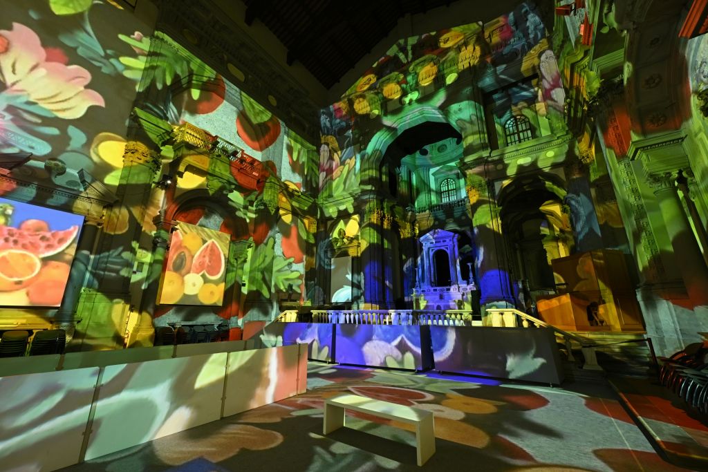 화려한 과일 테마의 조명 투영으로 조명이 켜진 교회 내부로, 전면에 흰색 벤치가 있습니다.