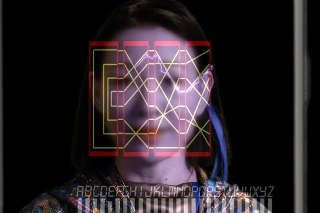 검은색 배경에 네온 기하학적 패턴과 알파벳 문자가 겹쳐진 사람의 얼굴.