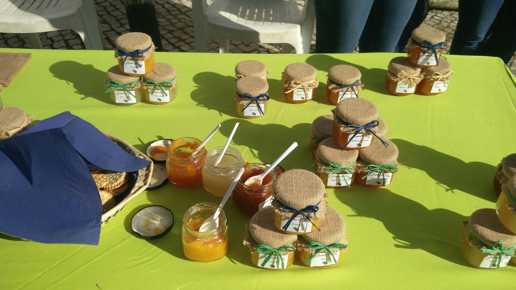 녹색 식탁보에 나무 뚜껑과 리본이 달린 잼 항아리가 있고, 항아리가 열려 있고 숟가락이 있습니다. 의자가 배경에 있습니다.