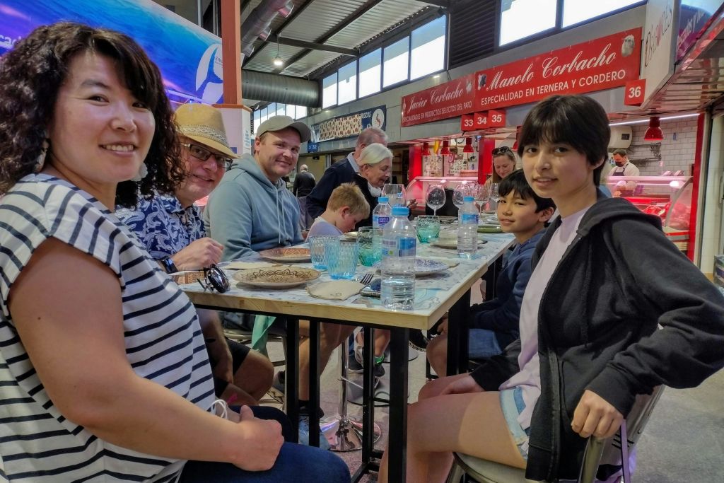 북적거리는 실내 시장이나 푸드 코트에서 음료와 접시가 놓인 테이블에 둘러앉은 사람들의 일행.