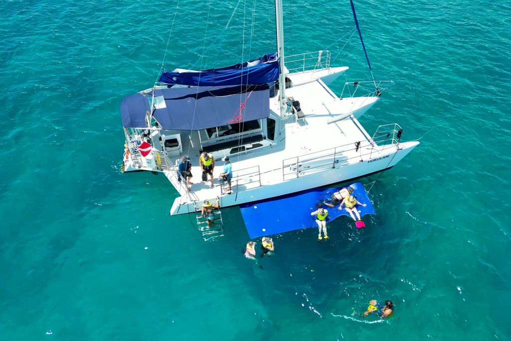 와이키키의 맑고 푸른 바다에서 호쿨라니 쌍동선에서 휴식을 취하고 스노클링을 즐기는 게스트.