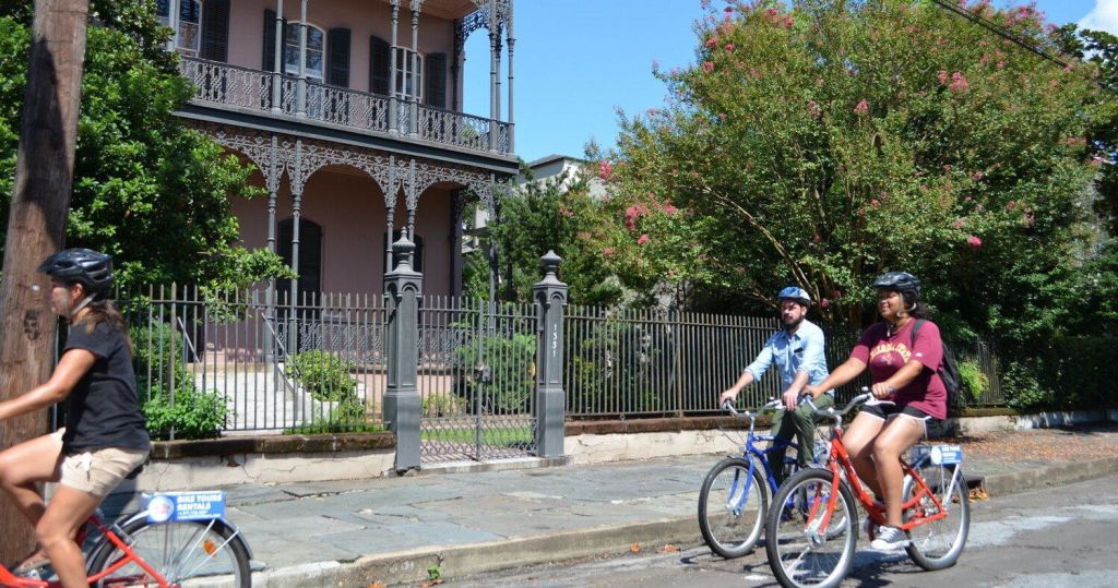 나무와 연철 울타리를 배경으로 햇살 가득한 거리에서 자전거를 타고 있는 두 사람.
