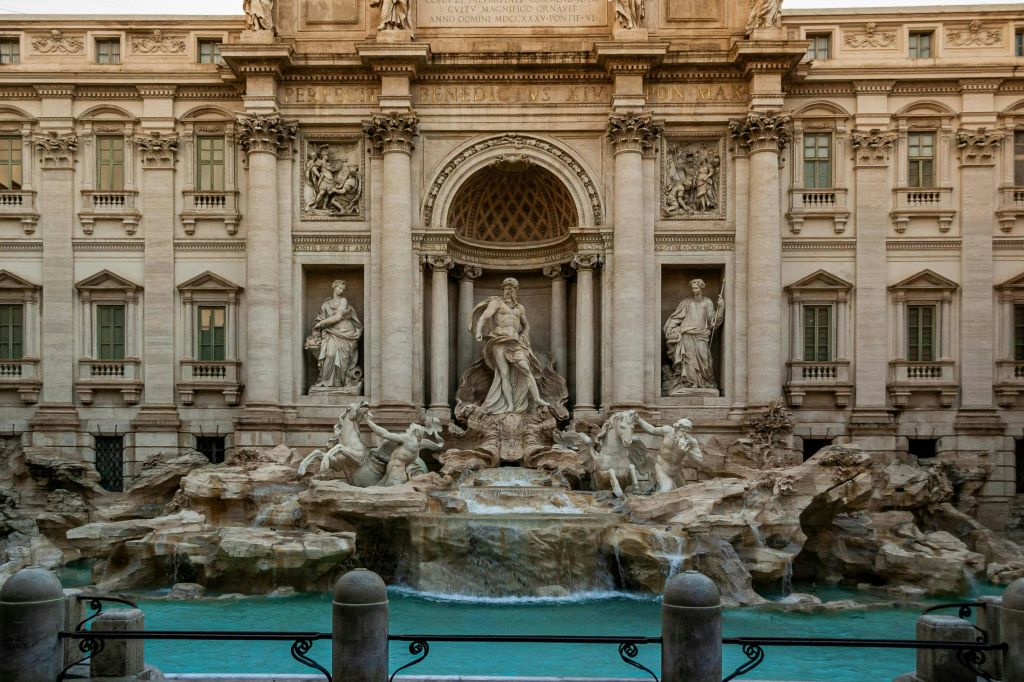 화려한 건축물을 배경으로 조각상, 기둥, 흐르는 물이 있는 웅장한 바로크 양식의 분수입니다.