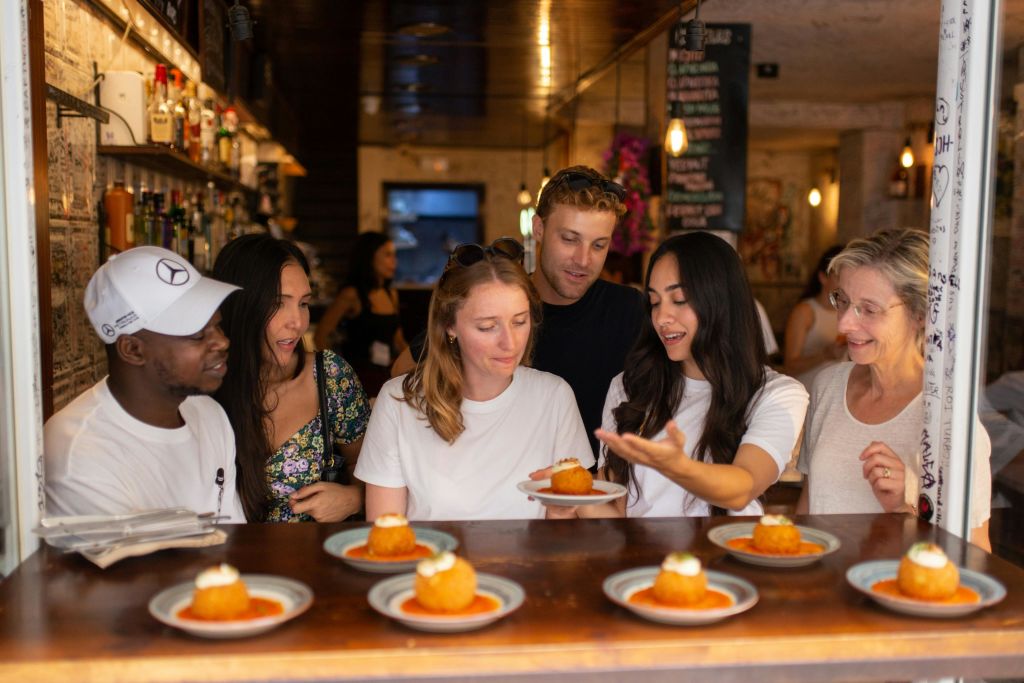 카운터에서 5명이 오렌지색 공 모양의 디저트가 담긴 접시를 보며 따뜻한 불을 밝힌 레스토랑 내부를 바라보고 있습니다.