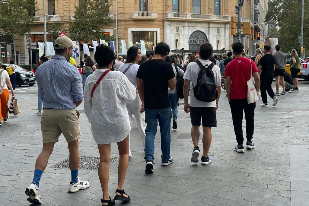 아치형 창문과 기둥이 있는 유서 깊은 건물 근처의 번화가를 걷는 사람들.