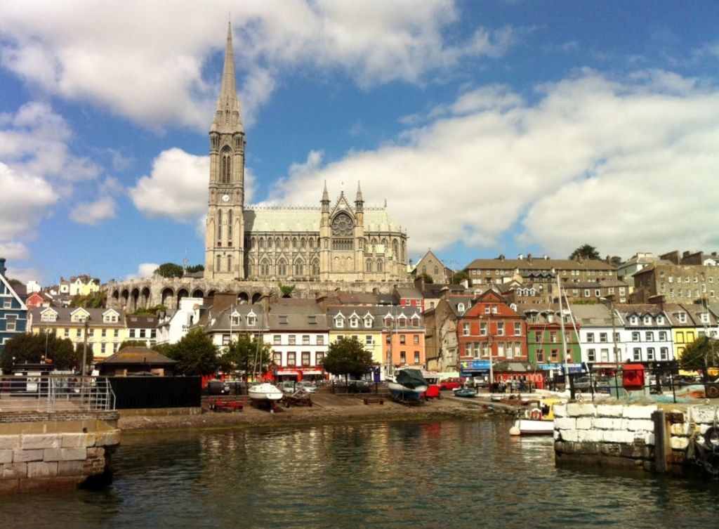 형형색색의 건물 위에 있는 커다란 대성당 타워와 보트가 부분적으로 흐린 하늘 아래 바닷가 근처에 정박해 있습니다.